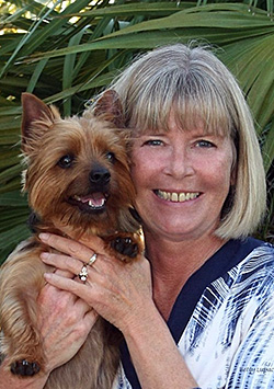 Bio photo of Denise Deisler, smling and holding a broan and black dog close to her face