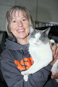 Bio photo of Dr. Sara Kirk, smiling in a dark gray hoodie, holding a gray and white cat