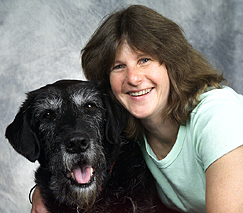 Bio photo of Dr. Tracy Stokol, smiling in a pale green shirt, embracing a large black dog