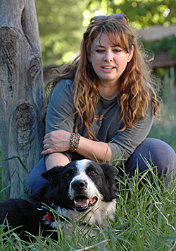 Bio photo of Liz Finch, kneeling in a wooded grassing setting with a black and white dog