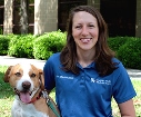 Bio photo of Dr. Staci Cannon smiling in a blue shirt, next to a large brown and white dog