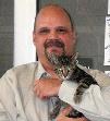 Bio photo of Scott Trebatoski in a white shirt, smiling and holding a small gray cat