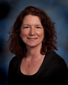 Bio shot of Dr. Elizabeth Berliner, smiling in a black shirt against a dark background