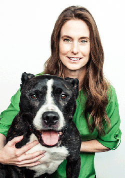Bio photo of Aimee Galbreath, smiling, im a green long sleeve shirt, holding a black and white dog