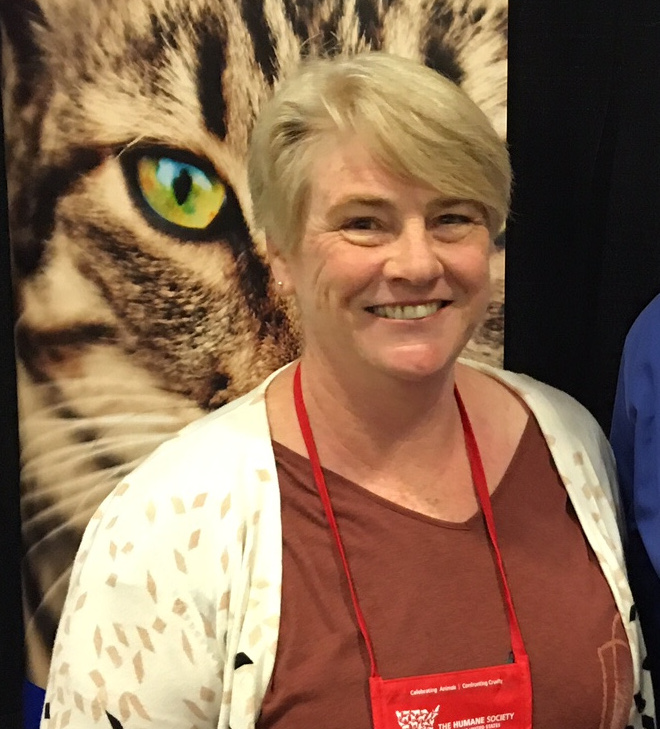 Bio photo of Dr. Ann Enright smiling in front of large cat poster at an industry event