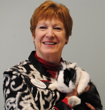 Bio photo of Kathleen Olson, smiling in a back and white shirt, holding a black and white cat