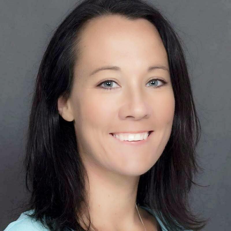 Bio portrait of Kristen Auerbach, smiling, in a light shirt against a dark background