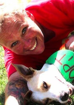 Bio photo of Maureen Keenan, laying in the grass, smiling with a reclining little white dog