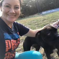 Bio photo of Dr. Alexis Bardzinski, smiling in a dar tee shirt, petting a black dog