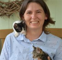 Bio photo of April Moore, smiling in a pale blue button-down shirt with two kittens