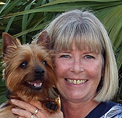 Bio photo of Denise Deisler, smiling in an outdoor setting, holding a brown and black terrier