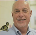 Bio photo o Don Bland, smiling in a pale blue dress shirt, with a duckling on his shoulder