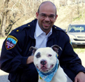 Bio photo of Ed Jamison, smiling in a blue coat, kneeling with a black and white dog.