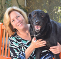 Bio photo of Gina Knepp, smiling in a blue, black and white patterned top, holding a big black dog