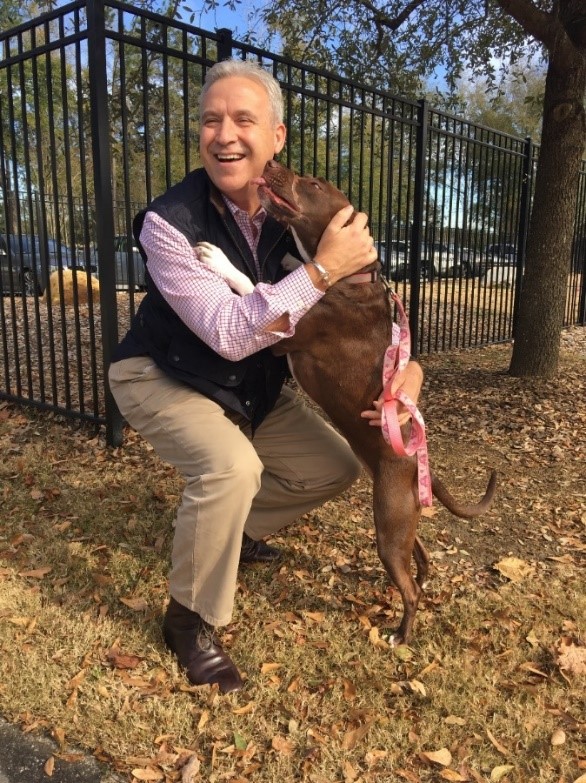 Bio photo of Joe Elmore, smiling, kneeling and hugging a black dog