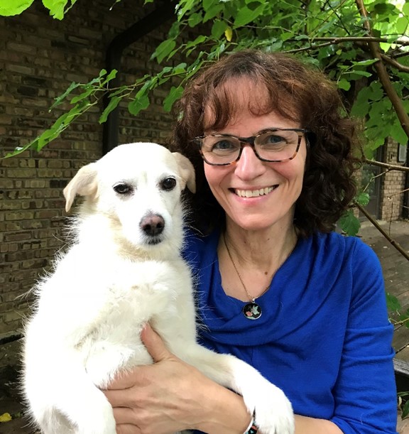 Bio photo of Linda Harper in a blue shirt, smiling and holding a little white dog