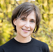 Bio portrait of Maggie Lynch, smiling in a black shirt in front of a leafy background