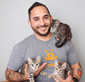 Bio photo of Marc Peralta, smiling ina gray tee shirt, holding three cats