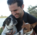 Bio photo of Mike Kaviani, in a dark shirt, smiling down at the two dogs he's holding