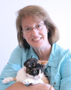 Bio portrait of Rosemarie Crawford, smiling in a pale blue shirt, holding a back and white cat