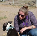 Bio photo of Sarah Aguilar, kneeling in an outdoor setting, talking to a black and white dog