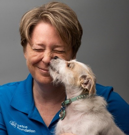 Bio photo of Sue Cosby smiling as a little white dog licks her face