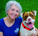 Bio photo of Teresa Johnson, smiling in a blue top, next to a brown and white dog, in an outdoor setting
