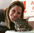 Bio photo of Monica Frenden smiling next to a tan and black cat