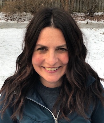 Bio photo of Aimee St.Arnaud, smiling in dark clothes in a wintry outdoors setting