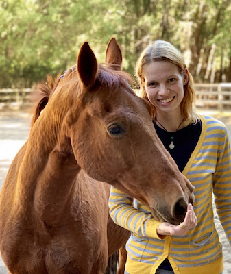 Bio photo of Carina DeVera smiling, standing next to a horse