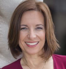 Bio photo of Sara Pizano smiling, in a burgandy shirt in a sunlit setting