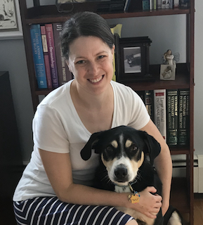 Bio photo of Dr. Erin Doyle, smiling and kneeling next to a black, tan and white dog