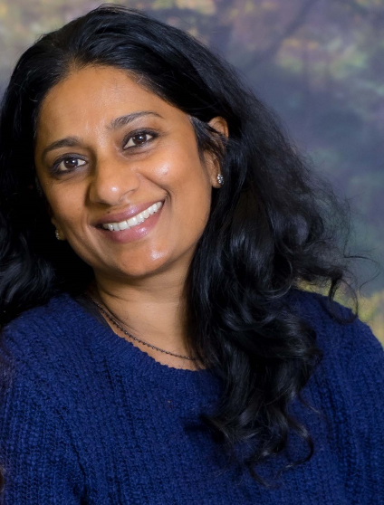 Bio portrait of Geraldine D'Silva, smiling in a dark blue shirt