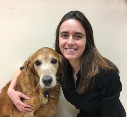 Bio photo of Dr. Jennifer Bolser, smiling and kneeling next to a brown and white dog