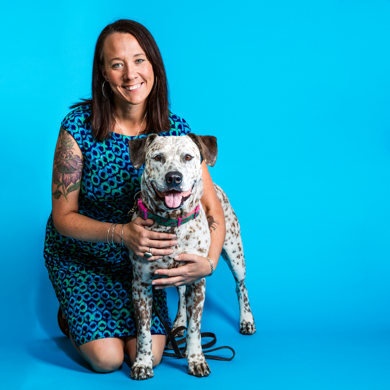 Bio photo of Dr. Kristen Hassen Auerbach, smiling, kneeling beside a spotted dog