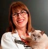 Bio photo of Dr. Annette Litster in a white lab coat, smiling and holding a white cat