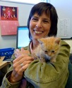 Bio photo of Dr. Kate Hurley, smiling in blue scrubs holding an orange cat