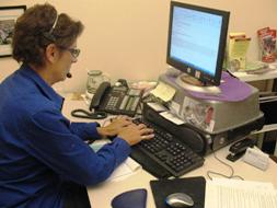 Person in a blue shirt and wearing a telephone headset, working on a computer