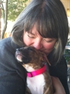 Bio photo of Christie Keith, kissing the top of a little black and white dog's head