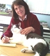 Bio photo of Barbara Carr sitting at a table in a burgundy sweater, smiling, petting a gray and white cat