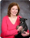 Bio photo of Dr. Kathleen Makolinski, smiling in a red sweater, holding a little back dog