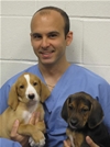 Bio photo of Dr.Brian A. DiGangi, smiling, wearing blue scrubs, holding two dogs